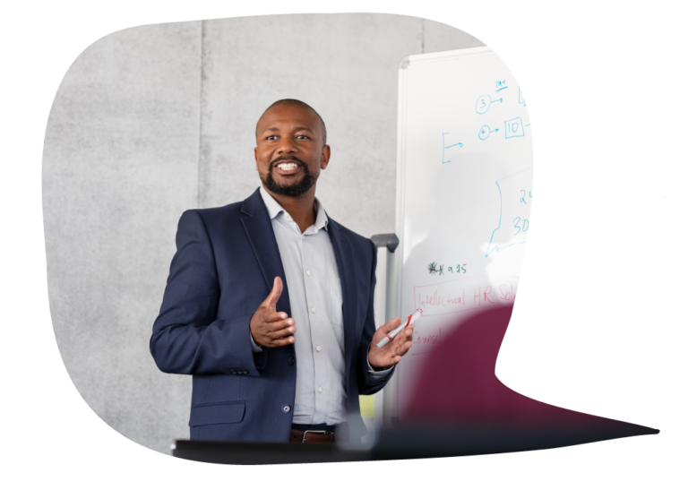 Professional man stands smiling next to a whiteboard as he gestures with his hands